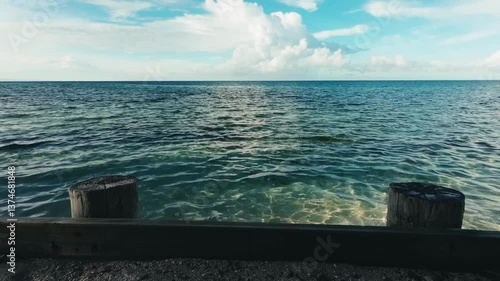 The ocean water tranquilly moving by a fishing pier with wooden barrier on a sunny day