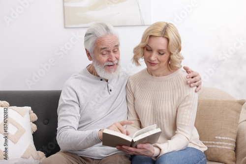 Senior man and mature woman reading book at home. Happy couple