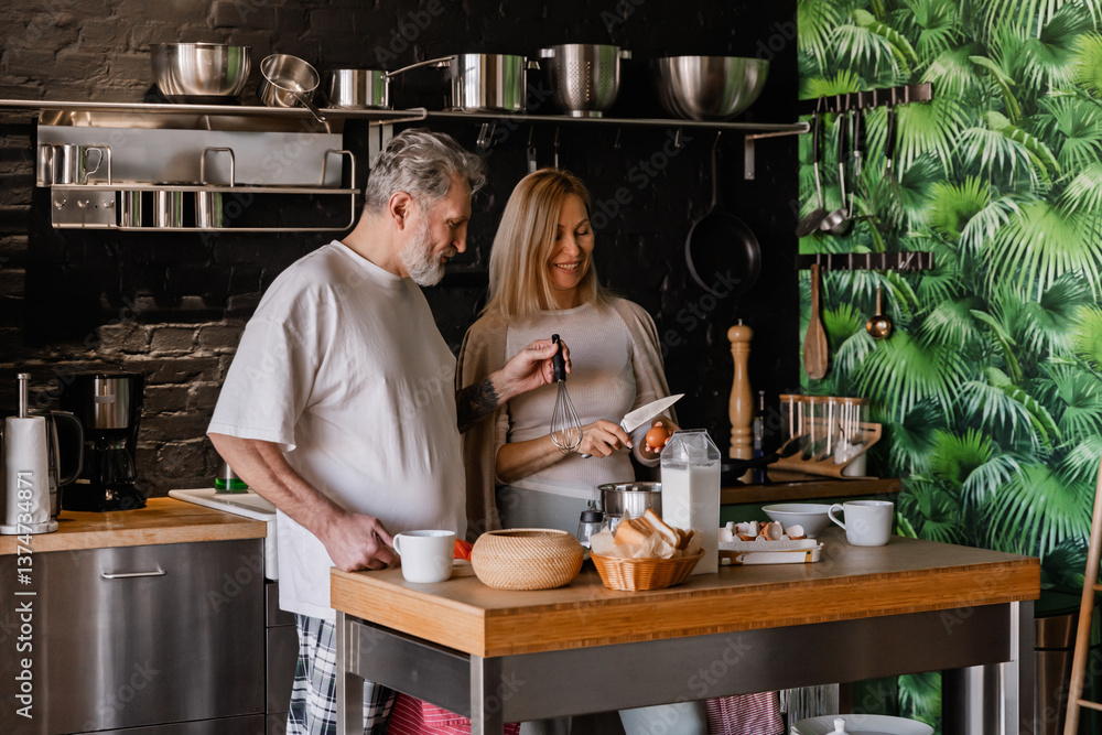 A White elder man with a tattoo and his wife with blonde hair are enjoying quality time together in their kitchen while also preparing breakfast and smiling at each other. A White elder man with a tattoo and his wife with blonde hair are enjoying quality time together in their kitchen while also preparing breakfast and smiling at each other.