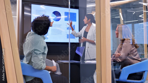 In a modern office, a woman presents data on a large screen to two colleagues, symbolizing effective teamwork and collaboration.