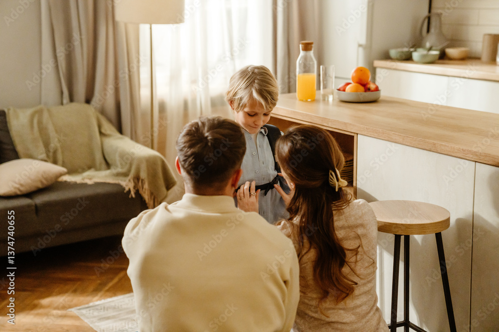 Φωτογραφία A White school-age boy with blonde hair, his father, his mother helping him get dressed in the kitchen while enjoying a warm and loving family moment together before starting their day