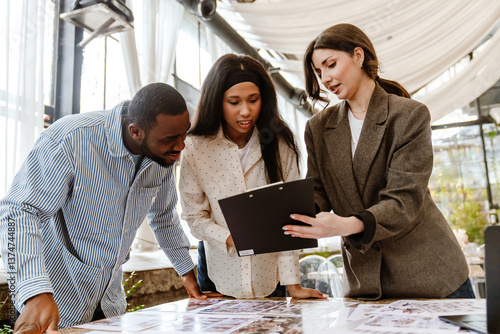 Foto A light-skinned female wedding planner shows a black planchette with info to a Black young couple in a cozy coffee afternoon
