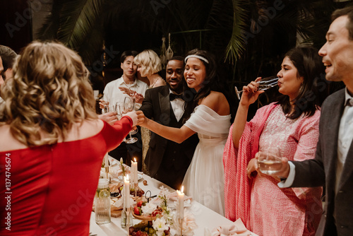 Obraz na plátně A Black groom and bride in a white dress toast with guests around a decorated wedding dinner table, holding champagne glasses and smiling during the celebration