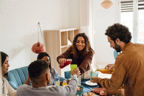 Photography A group of multiracial adult friends sitting around a table at home, pouring drinks and sharing food during an indoor gathering or celebration