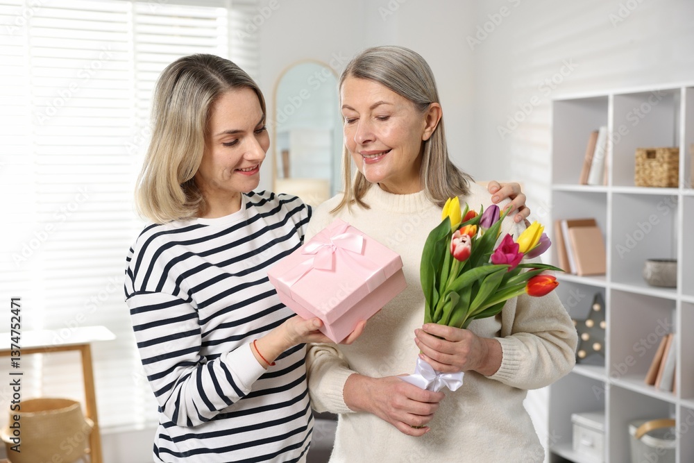 Smiling daughter congratulating her mom with bouquet of tulips and gift at home. Happy Mother's Day