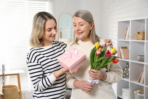 Obraz na płótnie Smiling daughter congratulating her mom with bouquet of tulips and gift at home. Happy Mother's Day w salonie