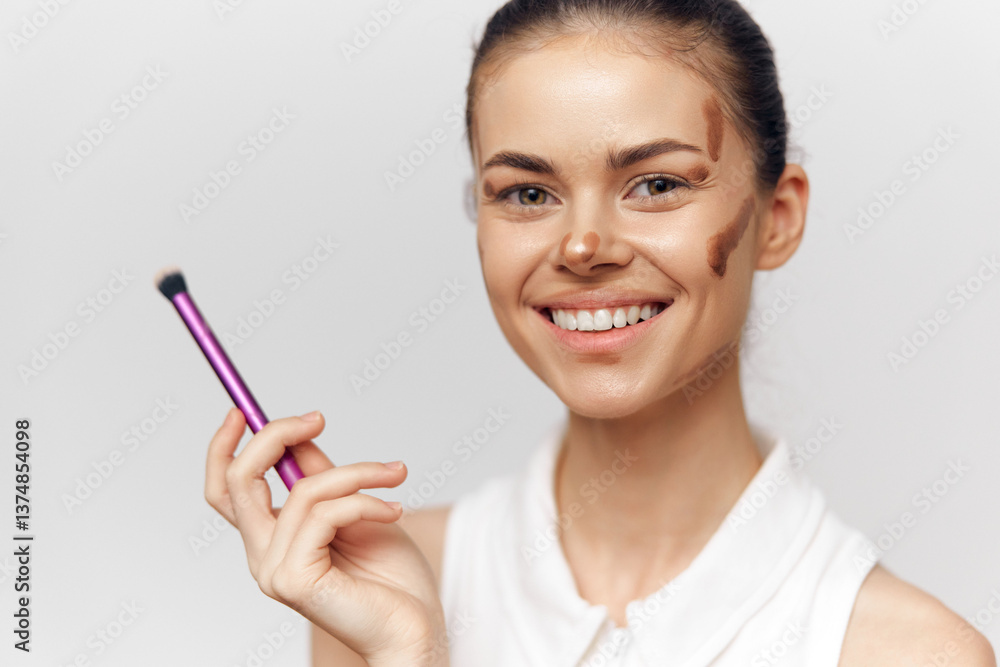 Young woman applying makeup with a brush, smiling joyfully, featuring a natural look and warm skin tones, set against a neutral background for beauty and fashion themes. Young woman applying makeup with a brush, smiling joyfully, featuring a natural look and warm skin tones, set against a neutral background for beauty and fashion themes.