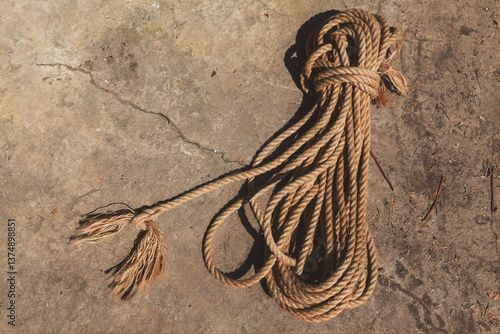 Obraz na płótnie Coiled rope resting on a rugged and weathered concrete surface. The rope, made of natural fibers, shows signs of wear with its frayed ends good for garden works w salonie