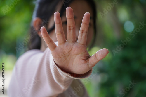 Young Girl Holding Hand Up in Stop Gesture Outdoors with Green Bokeh Background Showing Prevention and Protection