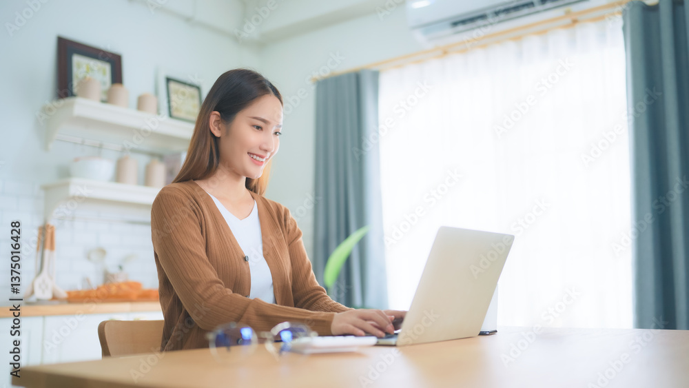 Obraz premium Beautiful young Asian woman working with laptop computer in home kitchen. Work at home