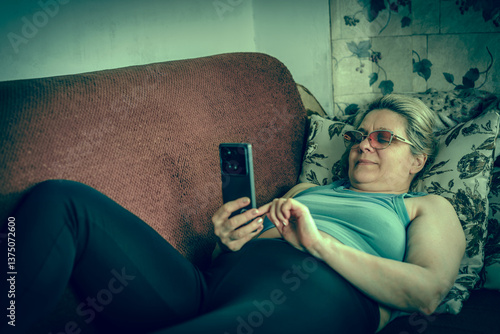 A woman is laying on a couch and using her cell phone