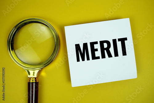 Merit text message written on paper note with magnifying glass top view on yellow background
