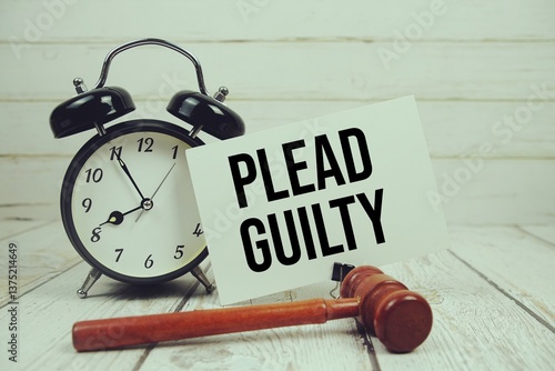 Plead Guilty text on paper card with alarm clock and wooden judge gavel on wooden background