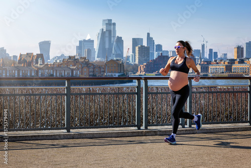 Obraz na płótnie A pregnant woman in sports clothing running for exercise in front of an urban skyline during a sunny day w salonie