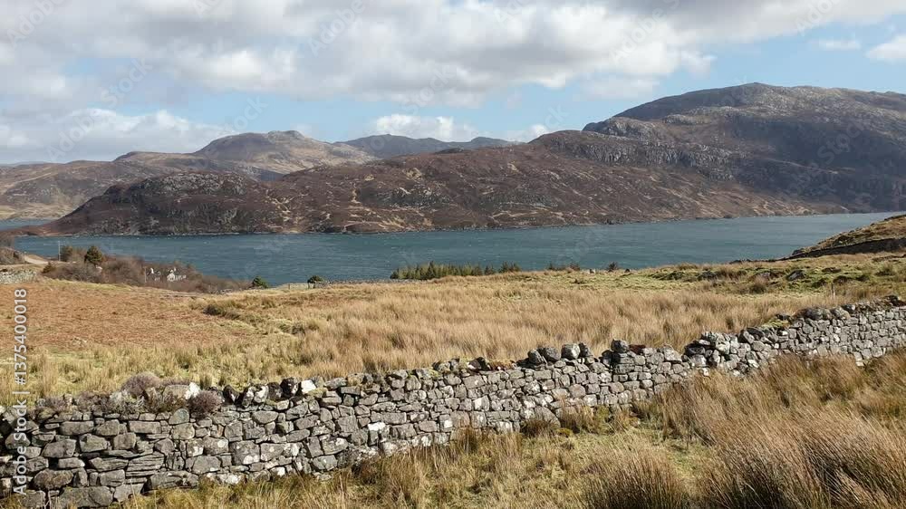 Scottish Outer Hebrides landscape view of rugged mountains, loch lake of water, tussock blowing in wind, and old stone wall in Scotland UK Scottish Outer Hebrides landscape view of rugged mountains, loch lake of water, tussock blowing in wind, and old stone wall in Scotland UK