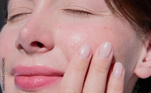 Принти на полотні Sunkissed close-up portrait of a beautiful woman gently touching her dewy cheek, highlighting a fresh, nourished, hydrated complexion and soft pink glow