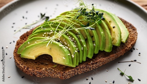 a perfectly sliced avocado is elegantly fanned out on top of a piece of whole grain toast lightly sprinkled with black sesame seeds and microgreens