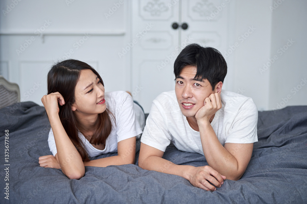 A young Asian couple is lying face down on a bed, smiling with happy expressions. A young Asian couple is lying face down on a bed, smiling with happy expressions.