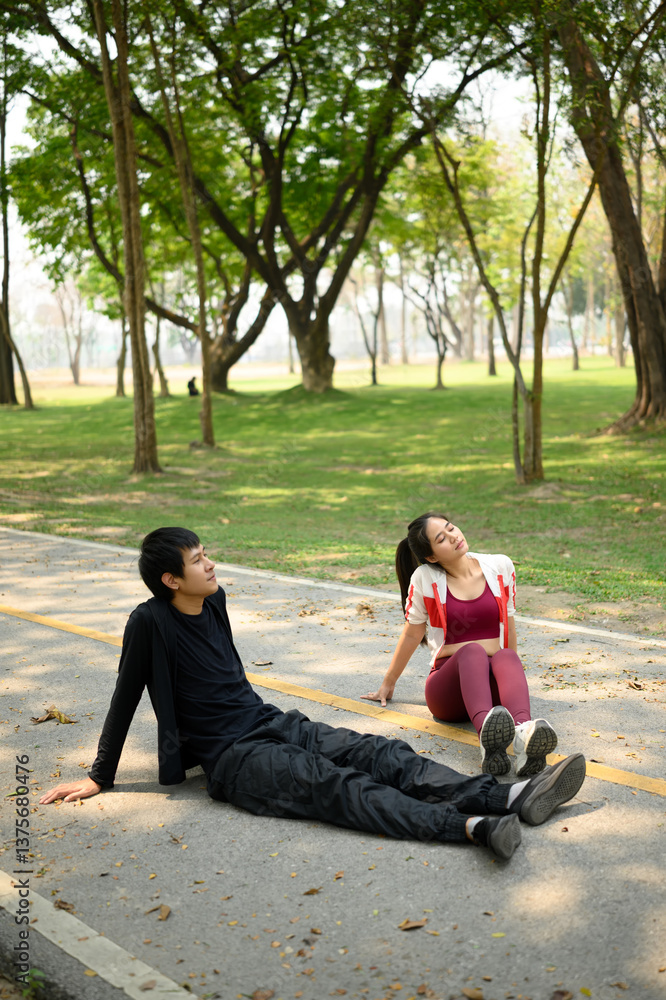 Tired man and woman sitting on a park pathway resting after a workout Tired man and woman sitting on a park pathway resting after a workout