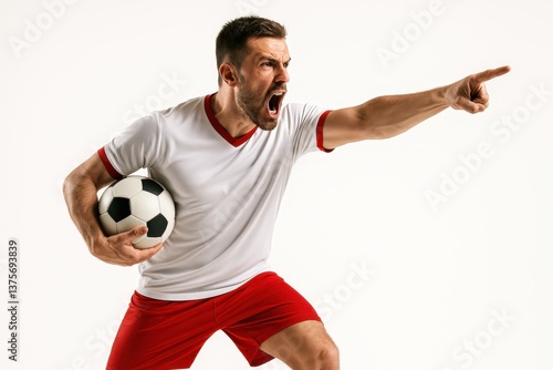 Emotional man, soccer player in red and white uniform shouting and pointing while holding ball on white background. Concept of sport, emotions, competition, leadership, action