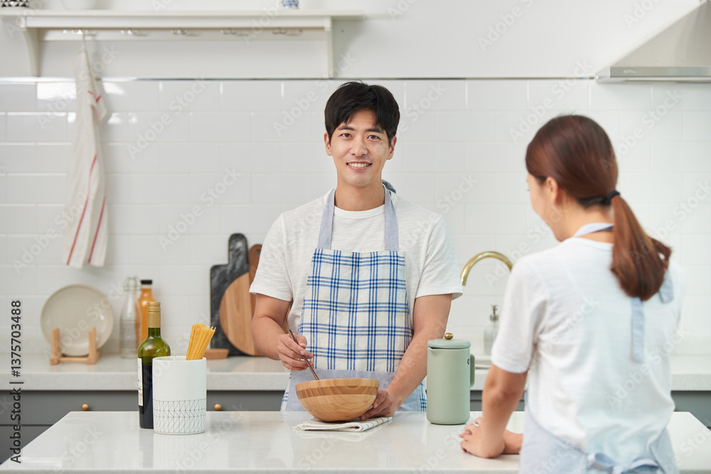 Fototapeta premium The young husband is cooking in the kitchen while having a pleasant conversation with his wife
