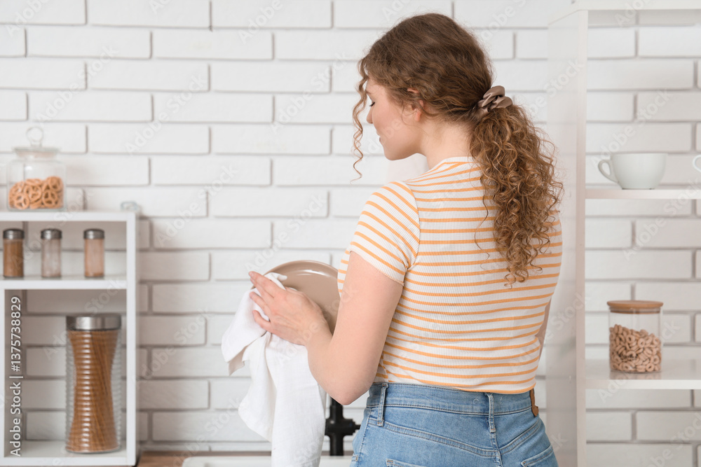 Naklejka premium Young woman wiping clean plate in kitchen, back view