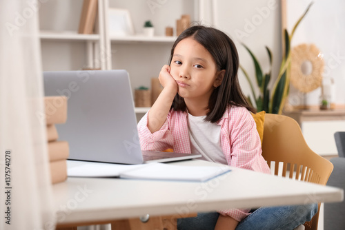 Upset little Asian girl with laptop studying online at home