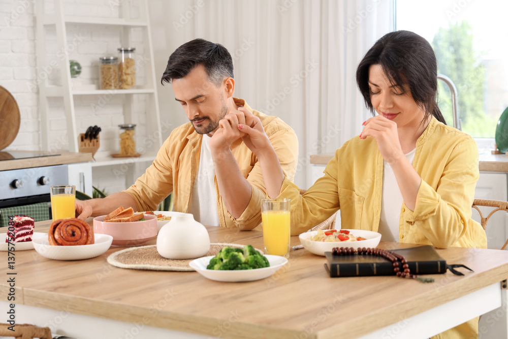 Religious couple praying before dinner at table in kitchen Religious couple praying before dinner at table in kitchen