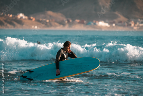 Photography Surfer carrying a surfboard on a beach, summer sunset surf scene