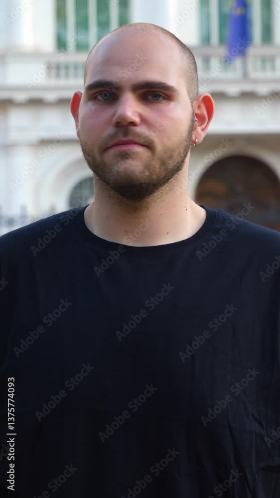 Vertical: A young bald man with a short beard looks serious in this portrait, capturing his intense gaze. Vertical: A young bald man with a short beard looks serious in this portrait, capturing his intense gaze.