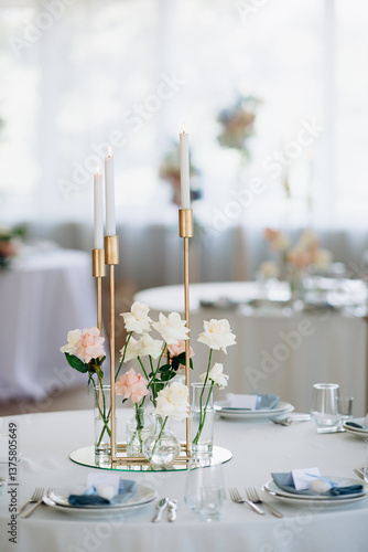 Many thin white candles in slender single candle holders burning on a banquet table in a restaurant, featuring pastel tones and a chic, minimalist atmosphere for a celebration or banquet