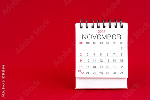 White desk calendar for November 2025 on red background.