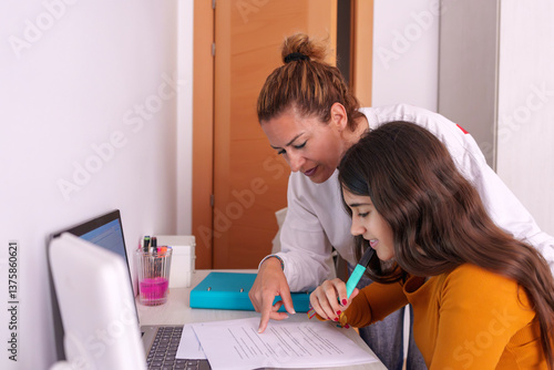 Mother guiding teenage daughter while reviewing homework at kitchen table