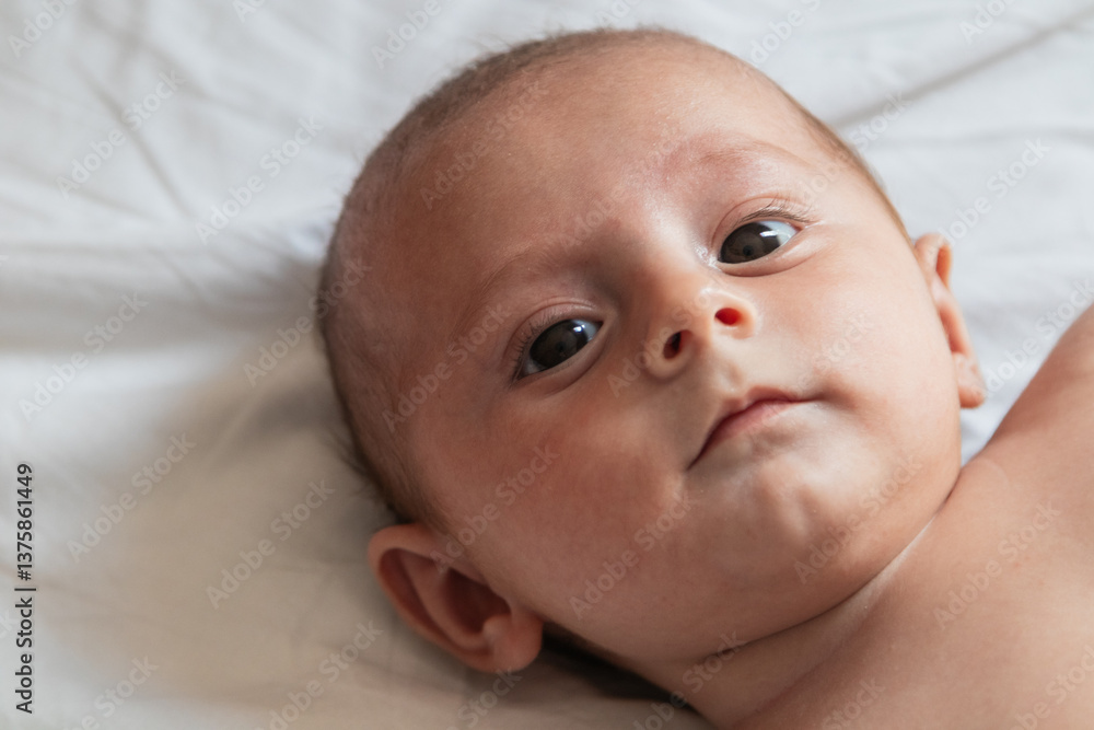 Four month old baby lying on white sheets making eye contact Four month old baby lying on white sheets making eye contact