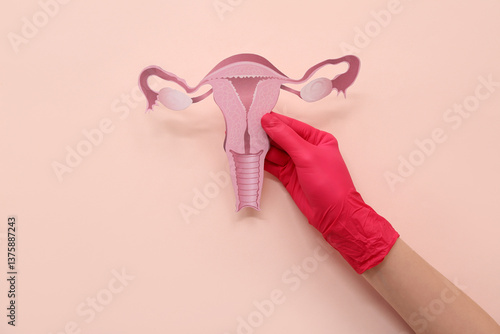 Doctor holding paper uterus on beige background