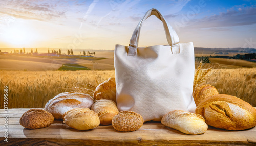 Obraz na płótnie natural beige canvas huge tote bag placed on a rustic wooden surface, surrounded by fresh breads varieties. w salonie