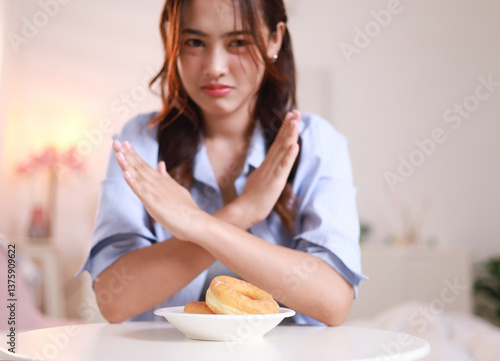 Фотография Young woman pushes hand away, rejects sugary donuts, donuts and sweets on plate,
