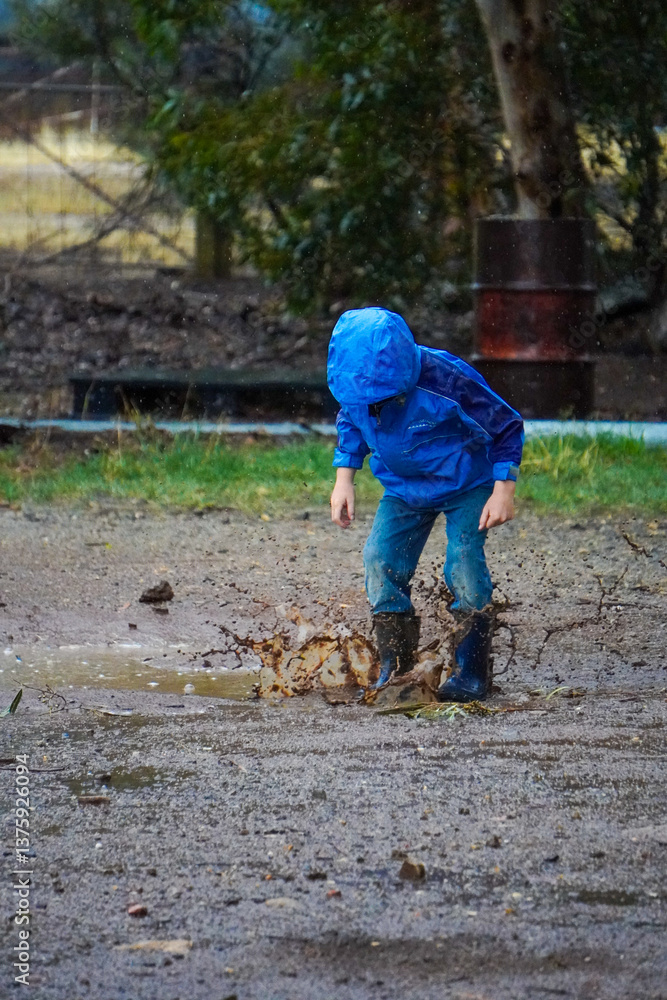 child in blue rain jacket jumping in muddy puddles child in blue rain jacket jumping in muddy puddles
