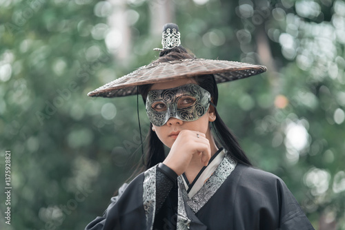 Chinese warriors wearing old traditional costumes. An elegant warrior in a conventional black robe holding a sword wearing a woven bamboo hat with mask in the forest. Ancient Chinese warrior.