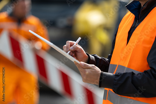 Construction worker in safety vest taking notes at a worksite during daytime