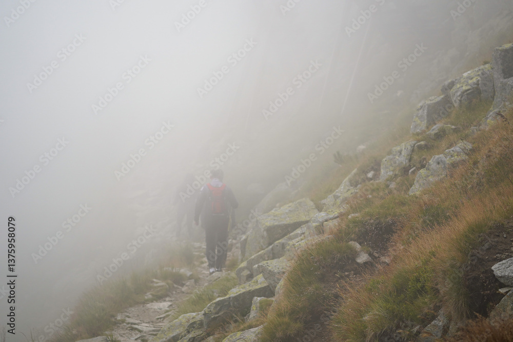 Obraz premium People hiking in a thick fog on top of the mountains on a rocky mountain slope path in High Tatra mountains, Slovakia