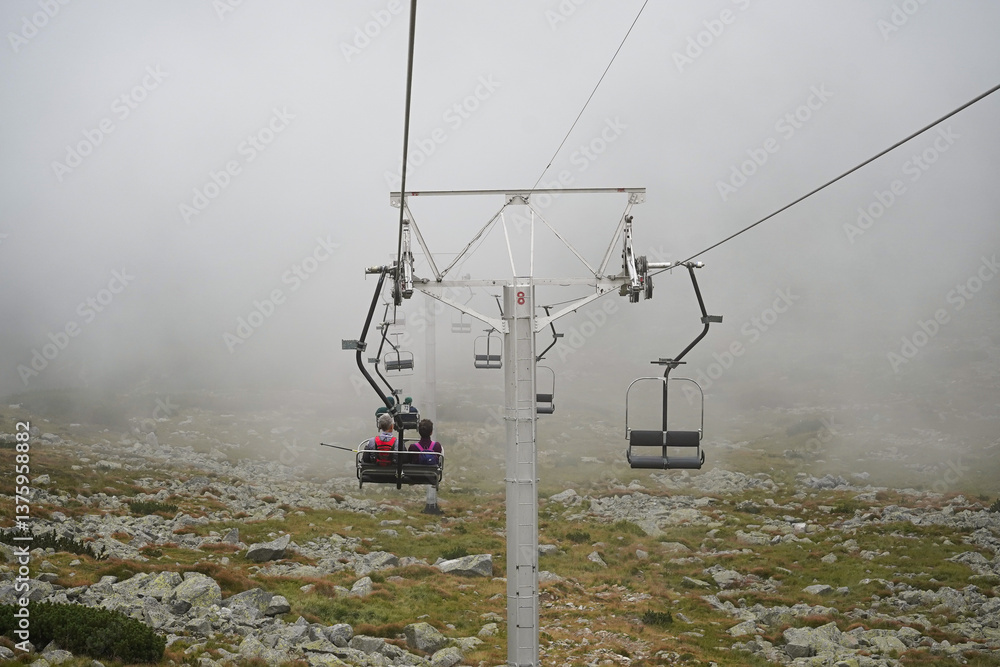 Mountain lift carrying people up a mountain with green plants on the bottom and grey cloud on top, High Tatra mountains, Slovakia Mountain lift carrying people up a mountain with green plants on the bottom and grey cloud on top, High Tatra mountains, Slovakia