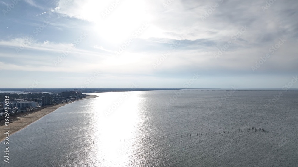 Virginia Beach, VA coastline at sunset with sandy beach and resorts with beach house by calm peaceful water reflecting sunlight Virginia Beach, VA coastline at sunset with sandy beach and resorts with beach house by calm peaceful water reflecting sunlight