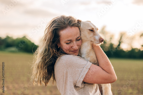 Happy woman hugging her dog in a field at sunset