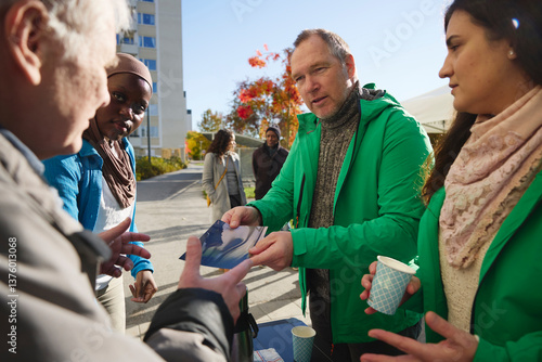 Mature male volunteer distributing flyer to man at park
