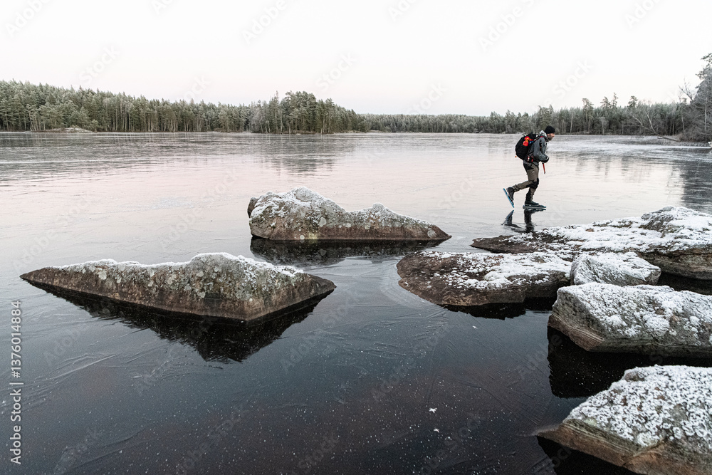 Man ice skating on frozen lake near rocks during winter against clear sky Man ice skating on frozen lake near rocks during winter against clear sky
