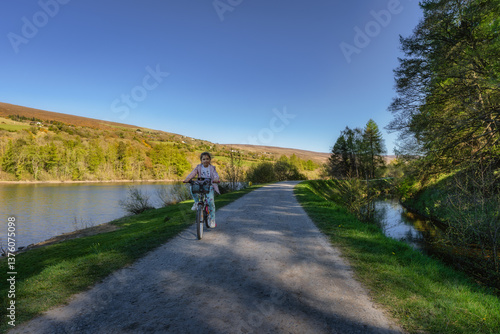 Obraz na płótnie A young girl joyfully rides her bicycle along beautiful, picturesque river pathway which is surrounded by vibrant autumn foliage, creating a serene atmosphere, Bohernabreena Reservoir, Dublin, Ireland w salonie