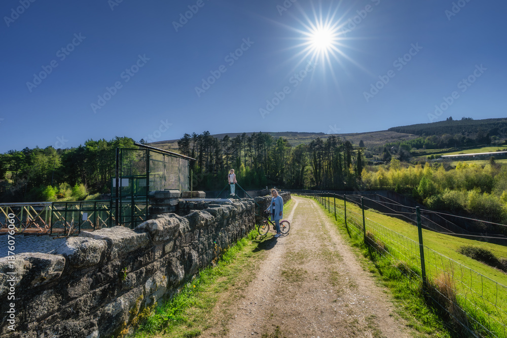 Mother and daughter on a bike, poses on colorful pathway under the sun, surrounded by lush greenery, perfect for outdoor adventures and enhance wellbeing, Bohernabreena Reservoir, Dublin, Ireland
