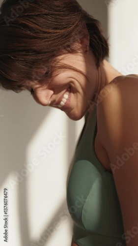 An active adult woman stands by a window with natural light, showcasing a beautiful smile, embodying health and a sporty lifestyle.