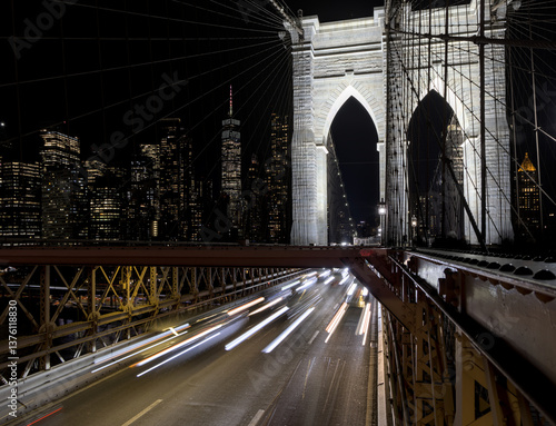cars driving over the brooklyn bridge at night (light trails long exposure headlights tail lights) manhattan new york city skyline background (dark sky) traffic congestion over east river crossing